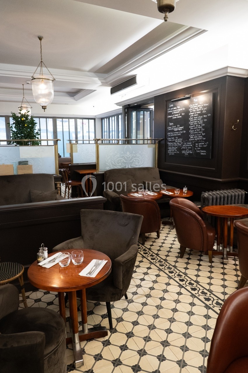 Salle de restaurant élégante avec tables en bois, fauteuils en cuir, carrelage à motifs et tableau noir au mur.