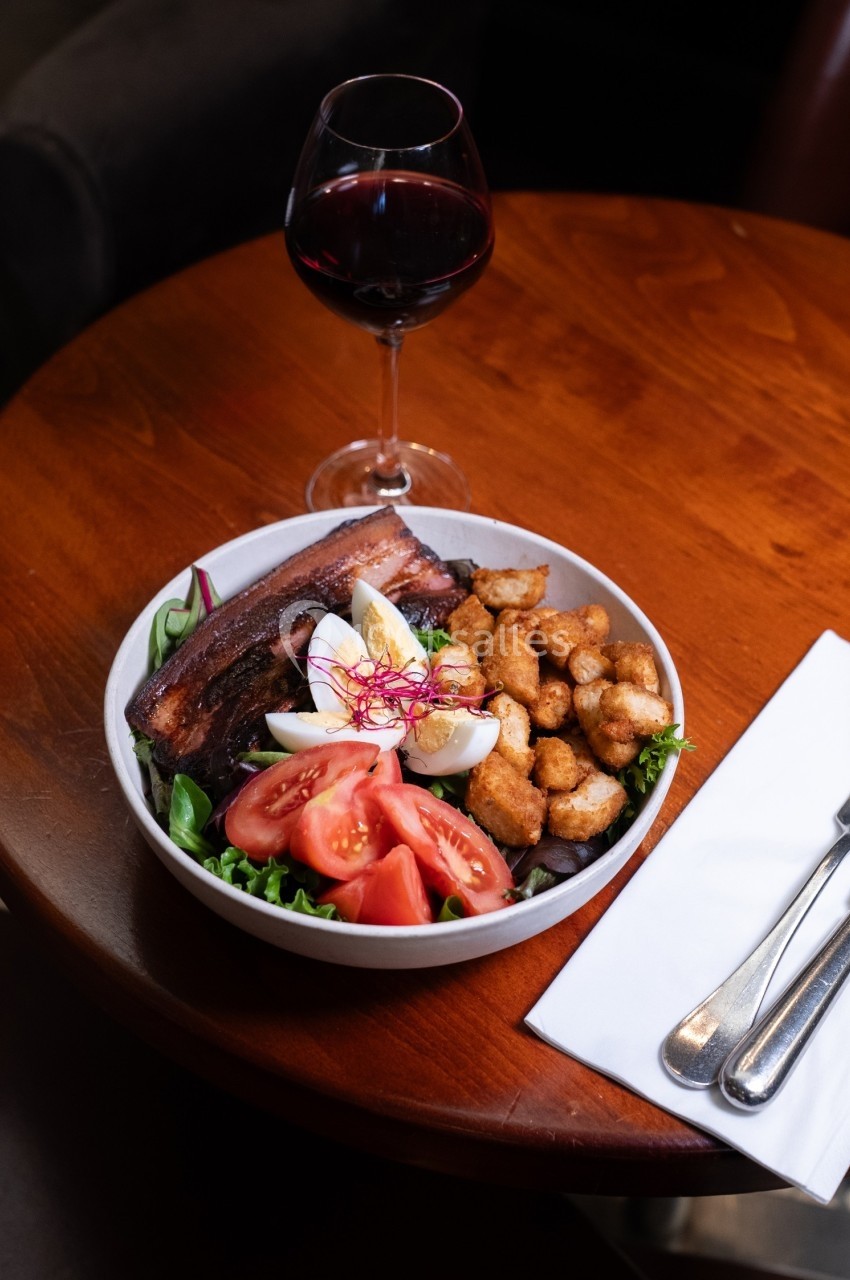 Assiette garnie de salade, tomates, œuf, morceaux de viande et croûtons, accompagnée d'un verre de vin rouge.