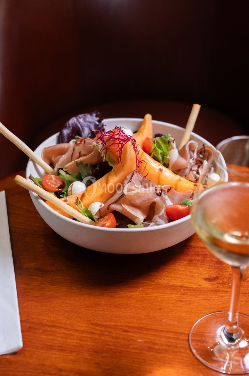 Salade composée avec jambon, melon, tomates cerises, mozzarella et feuilles de salade, servie dans un bol blanc.