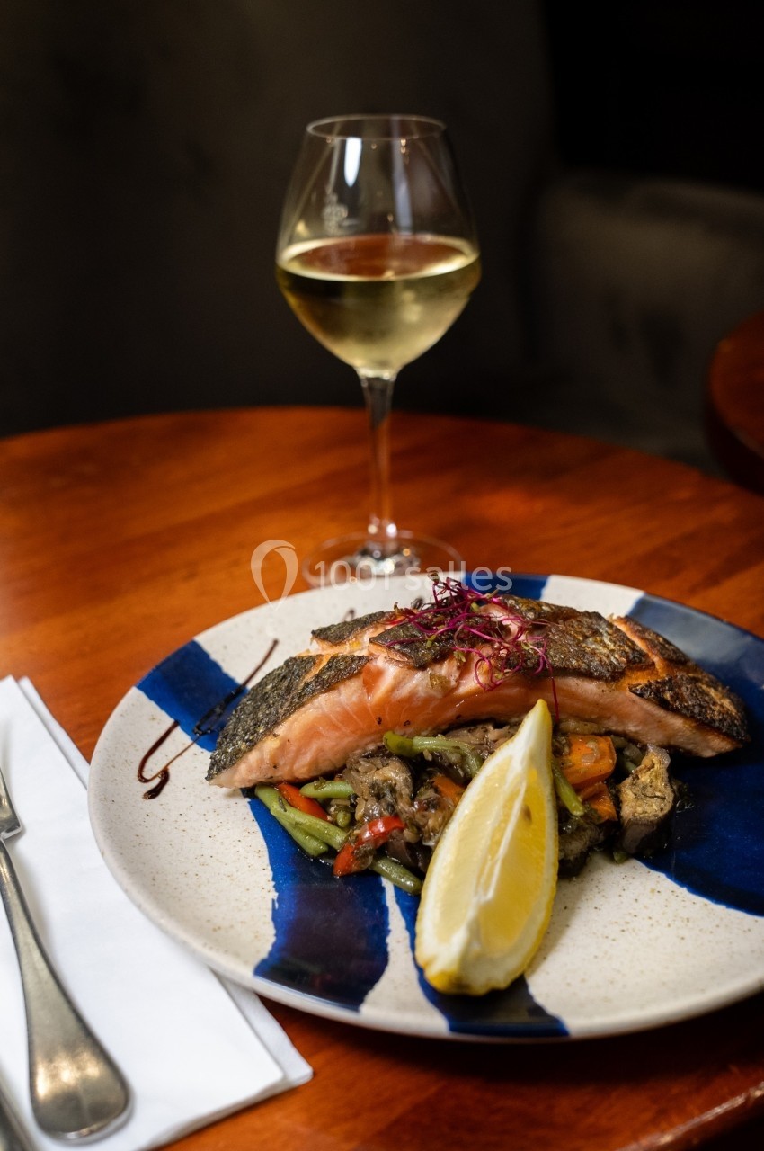 Assiette de saumon grillé avec légumes sautés, tranche de citron et verre de vin blanc sur une table en bois.