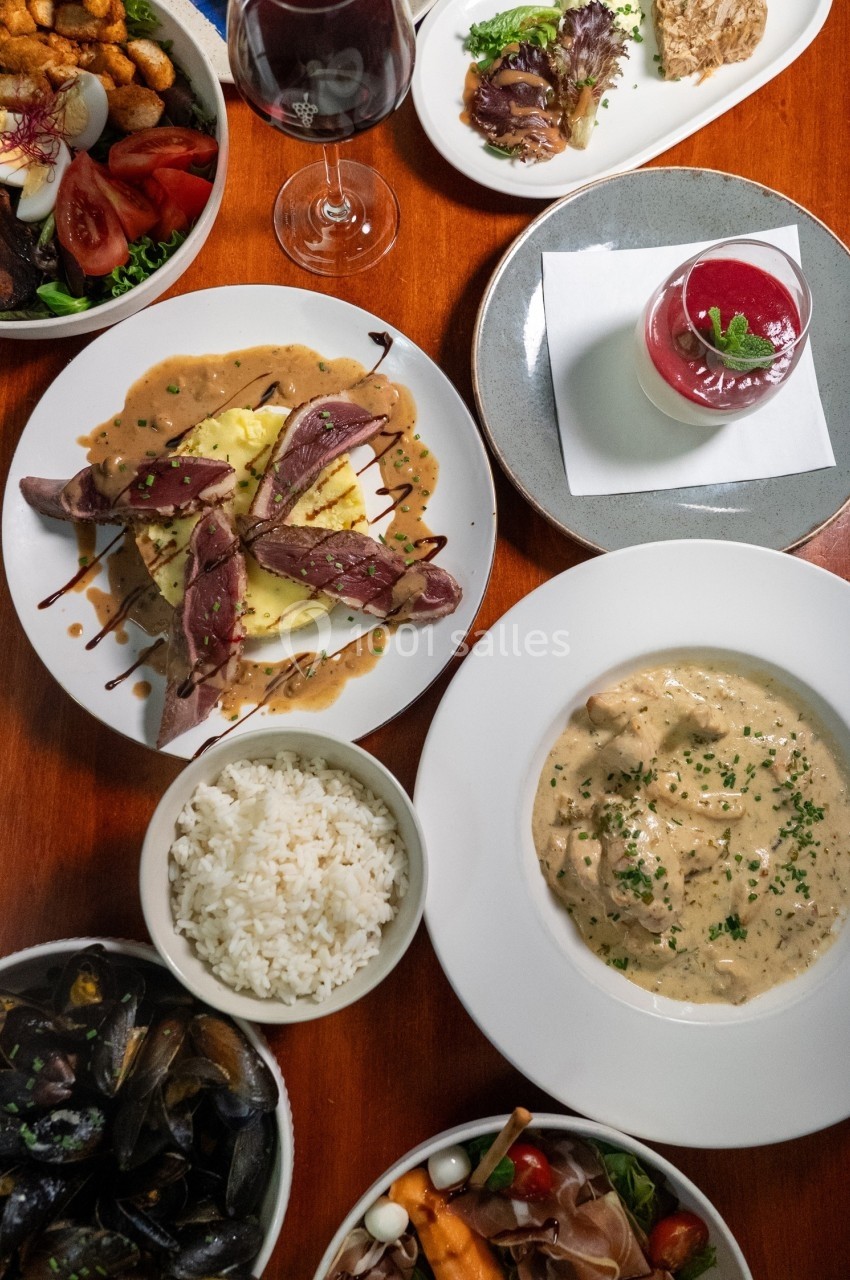 Table dressée avec divers plats : viande, moules, riz, salade, dessert et verre de vin rouge.