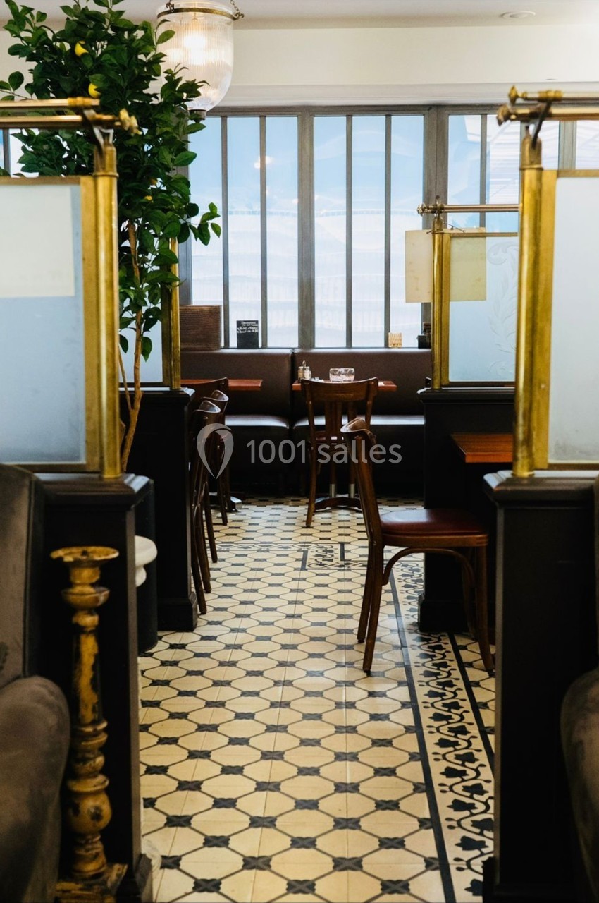 Salle de restaurant avec carrelage vintage, tables en bois et banquettes, éclairée par une grande baie vitrée.