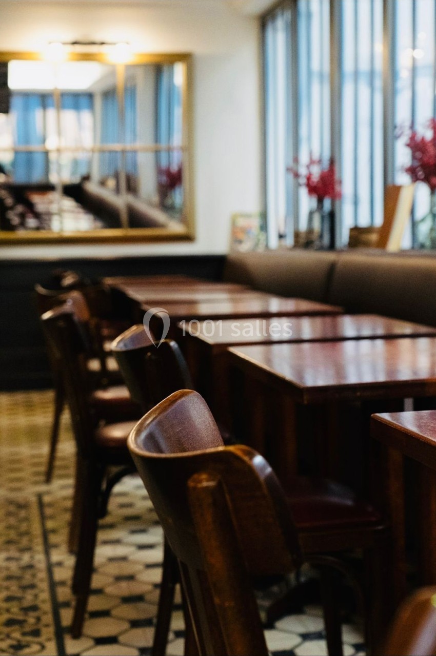 Salle de restaurant avec tables en bois, chaises assorties et grandes fenêtres laissant entrer la lumière naturelle.