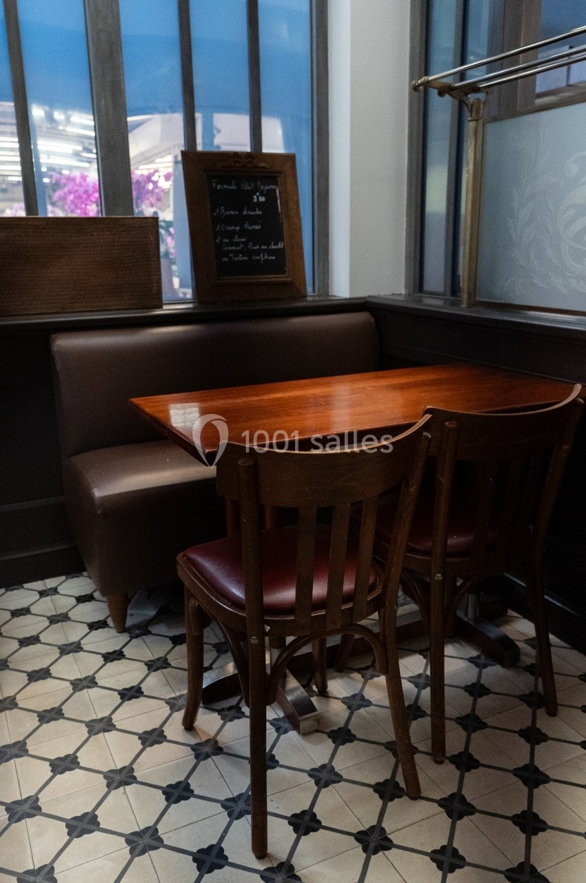 Table en bois avec deux chaises dans un coin de restaurant, près d'une banquette et d'une fenêtre.