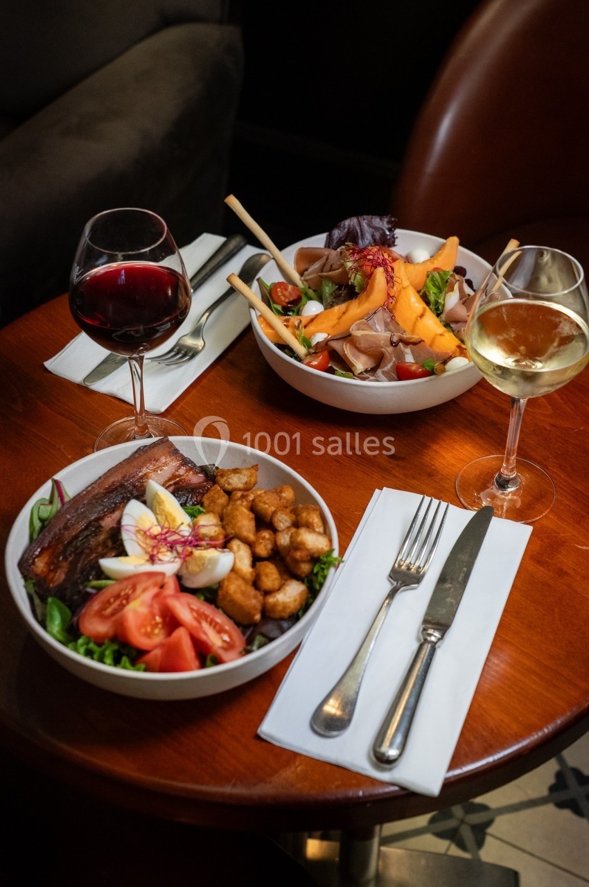 Deux assiettes garnies de salades variées avec verres de vin rouge et blanc, disposées sur une table en bois.