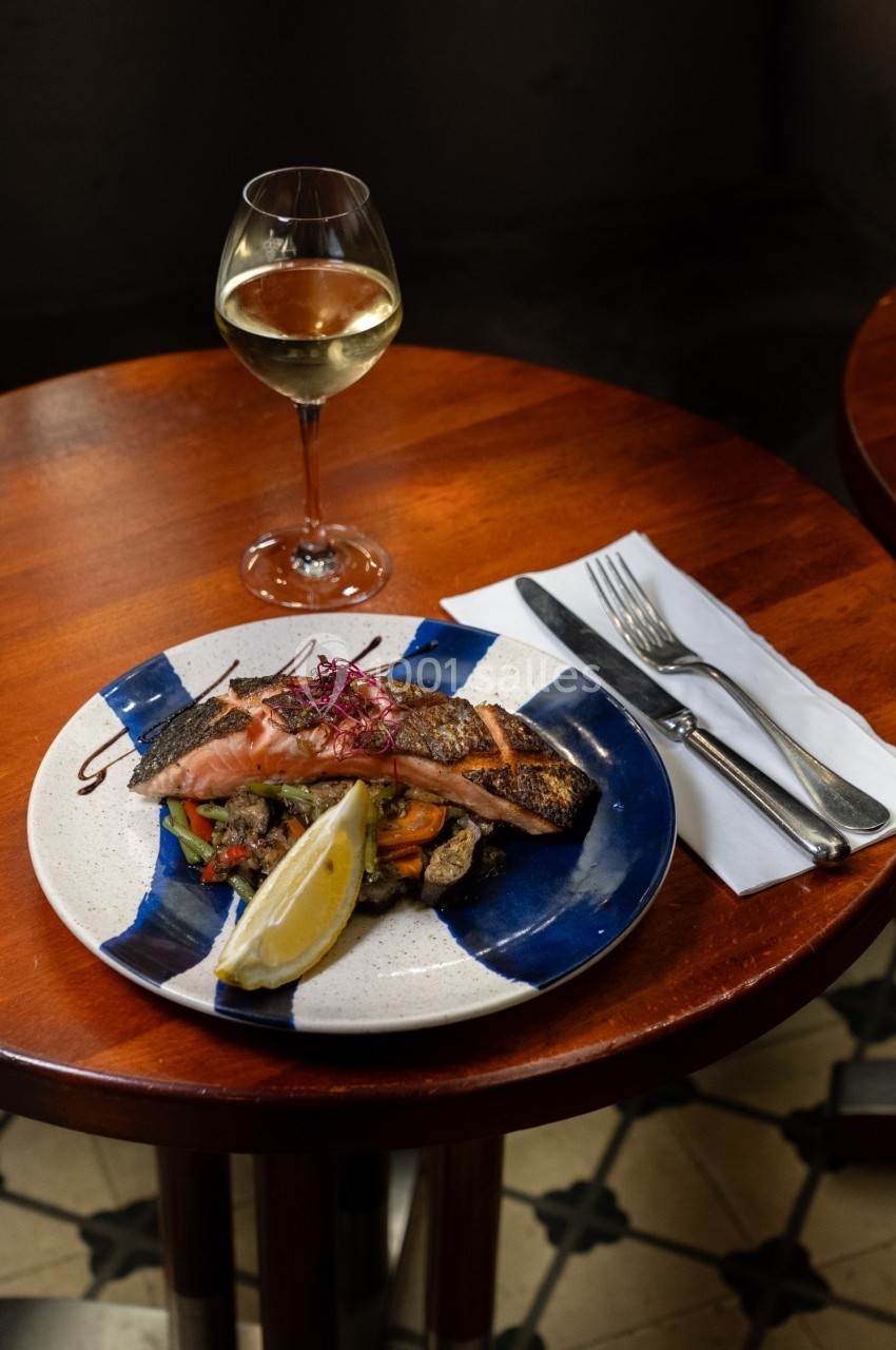 Assiette de saumon grillé avec légumes et citron, servie sur une table en bois, accompagnée d'un verre de vin blanc.