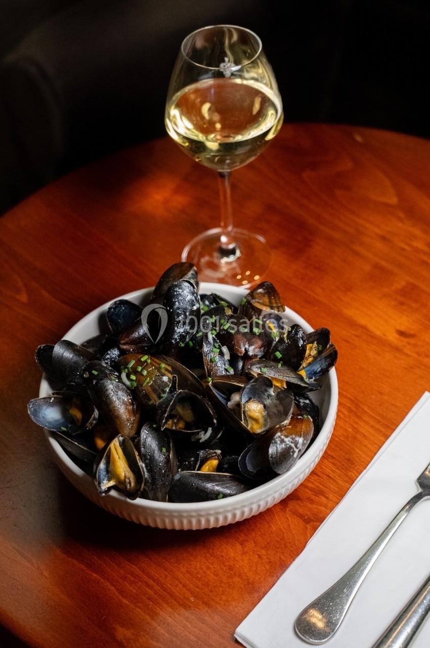 Assiette de moules cuisinées servie sur une table en bois avec un verre de vin blanc et des couverts.