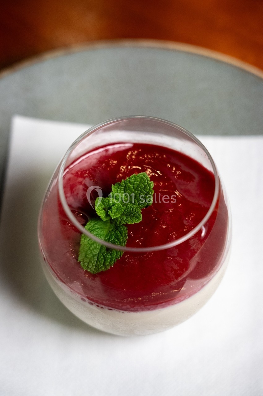 Verre de panna cotta surmontée d'un coulis rouge et décorée de feuilles de menthe, posé sur une serviette blanche.