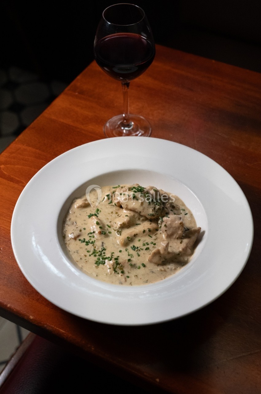 Assiette de blanquette de veau servie avec une sauce crémeuse, garnie de ciboulette, accompagnée d'un verre de vin rouge.