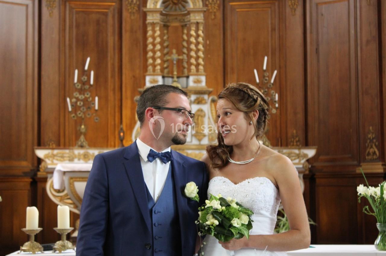 Un couple de mariés échange un regard complice devant l'autel d'une église ornée de bois sculpté.