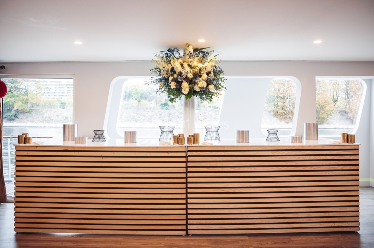 Comptoir en bois clair décoré d'un grand bouquet de fleurs blanches et jaunes, avec des photophores métalliques.