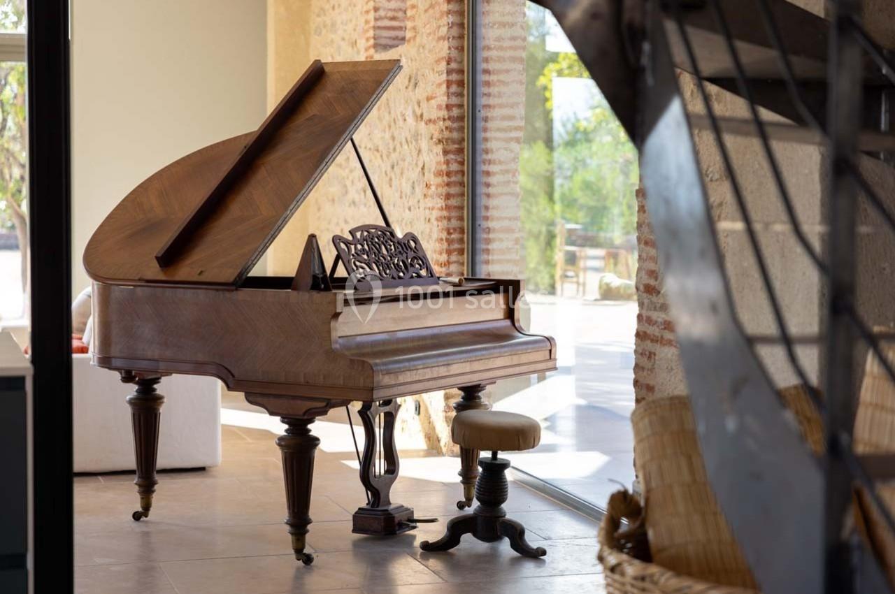 Piano à queue en bois avec tabouret, placé près d'une grande baie vitrée dans une pièce lumineuse.