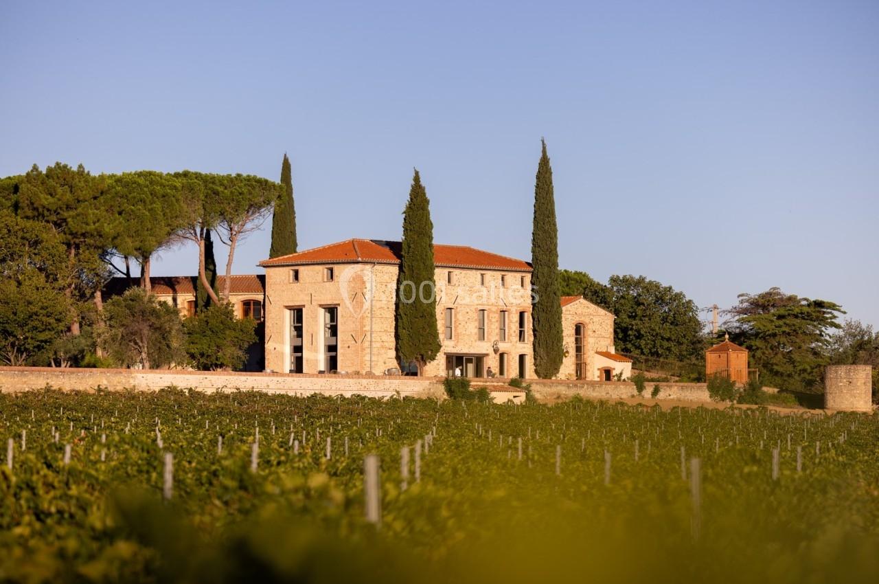 Bâtisse en pierre entourée de cyprès et de vignes sous un ciel dégagé.