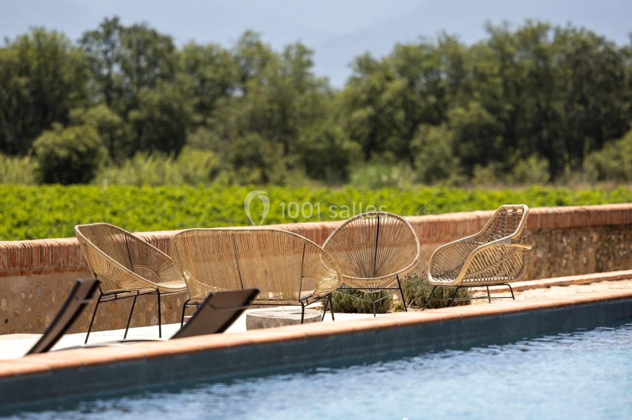 Chaises en rotin disposées près d'une piscine avec vue sur des collines boisées et des montagnes à l'horizon.
