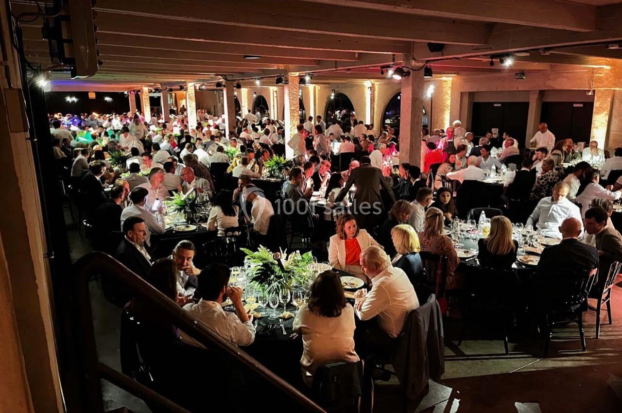 Salle remplie de convives assis à des tables rondes, éclairée par une lumière chaleureuse lors d'un événement.