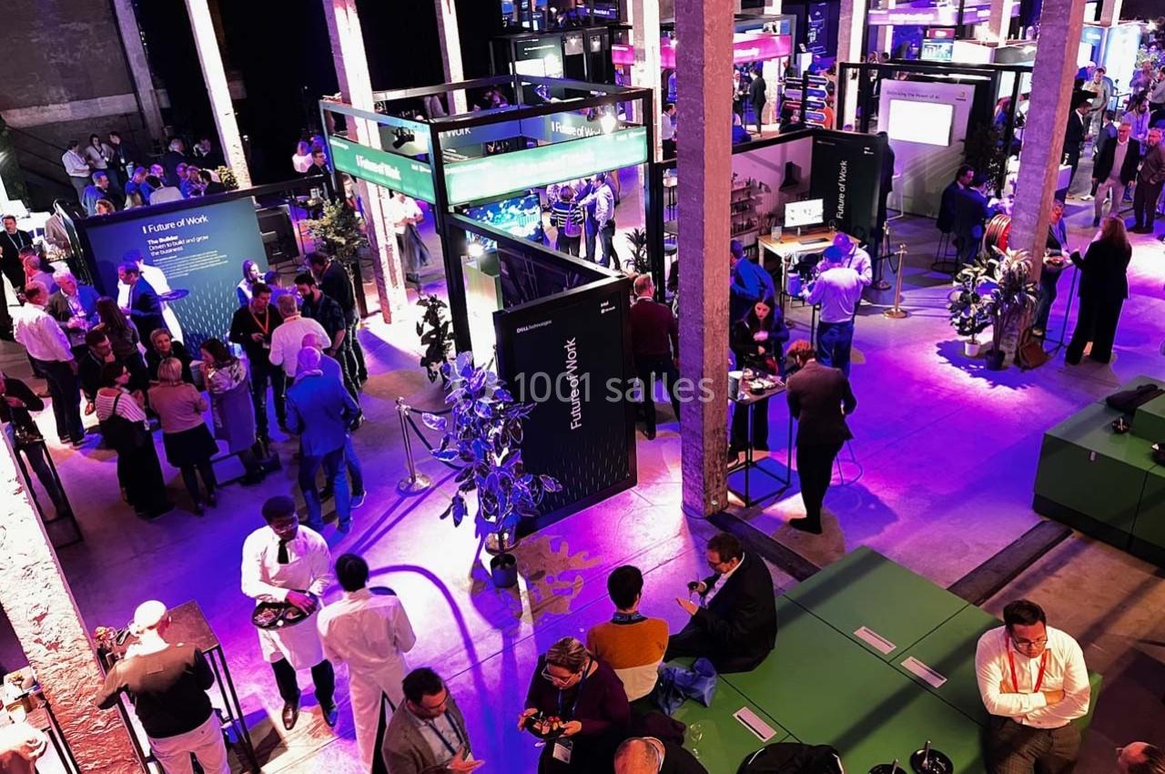 Vue d'un événement professionnel en intérieur avec des stands éclairés, des participants et une ambiance animée.