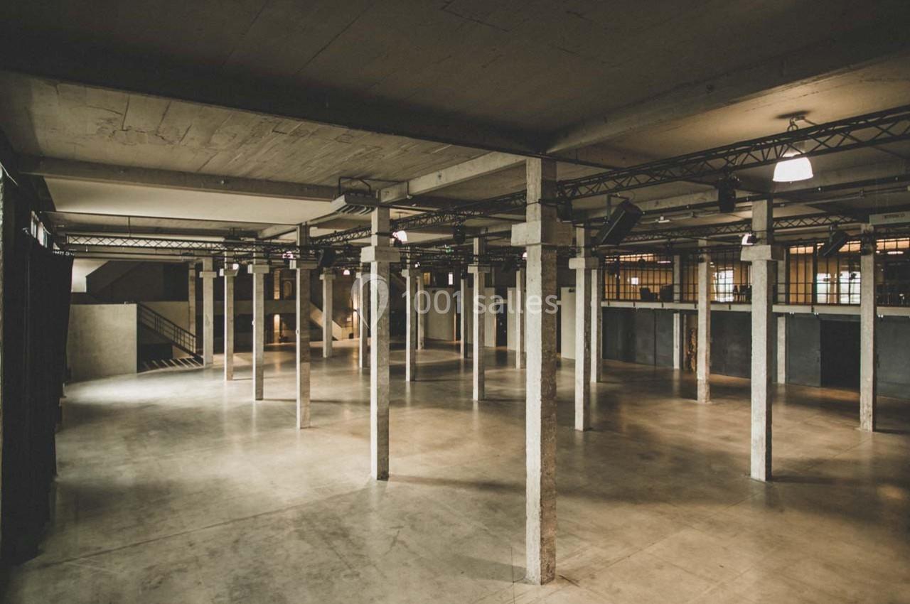 Vue d'un grand espace industriel vide avec des colonnes en béton, un sol en béton poli et un éclairage tamisé.
