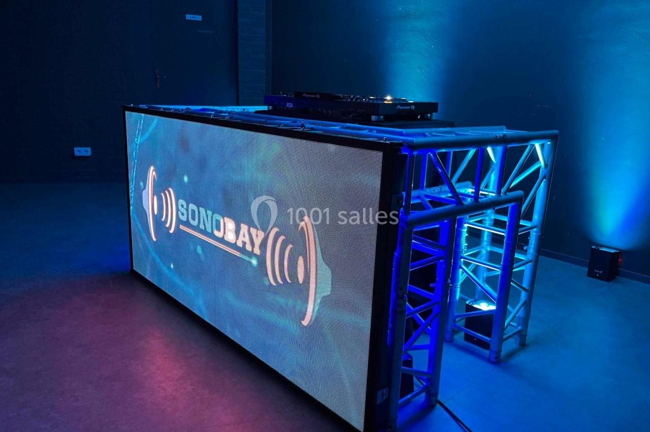Console de DJ avec écran LED affichant un logo lumineux, entourée d'une structure métallique et éclairée en bleu.