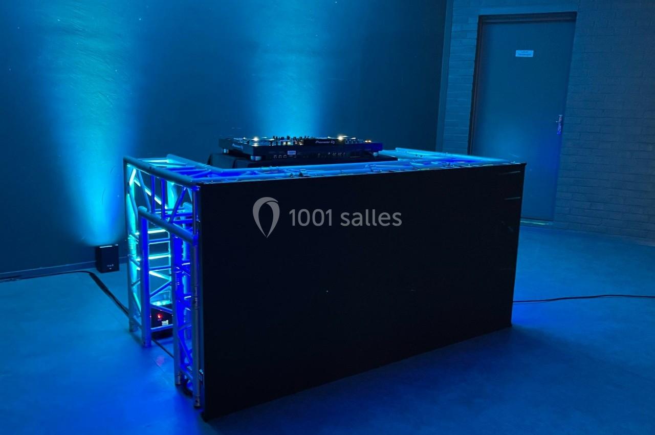 Table de mixage sur une scène éclairée par des lumières bleues, dans une pièce sombre avec une porte en arrière-plan.