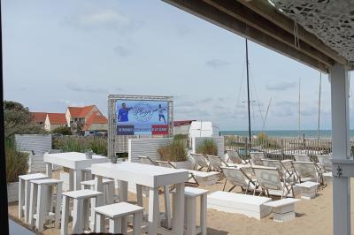 Terrasse en bord de mer avec tables et chaises blanches, vue sur la plage, la mer et un écran affichant une publicité.
