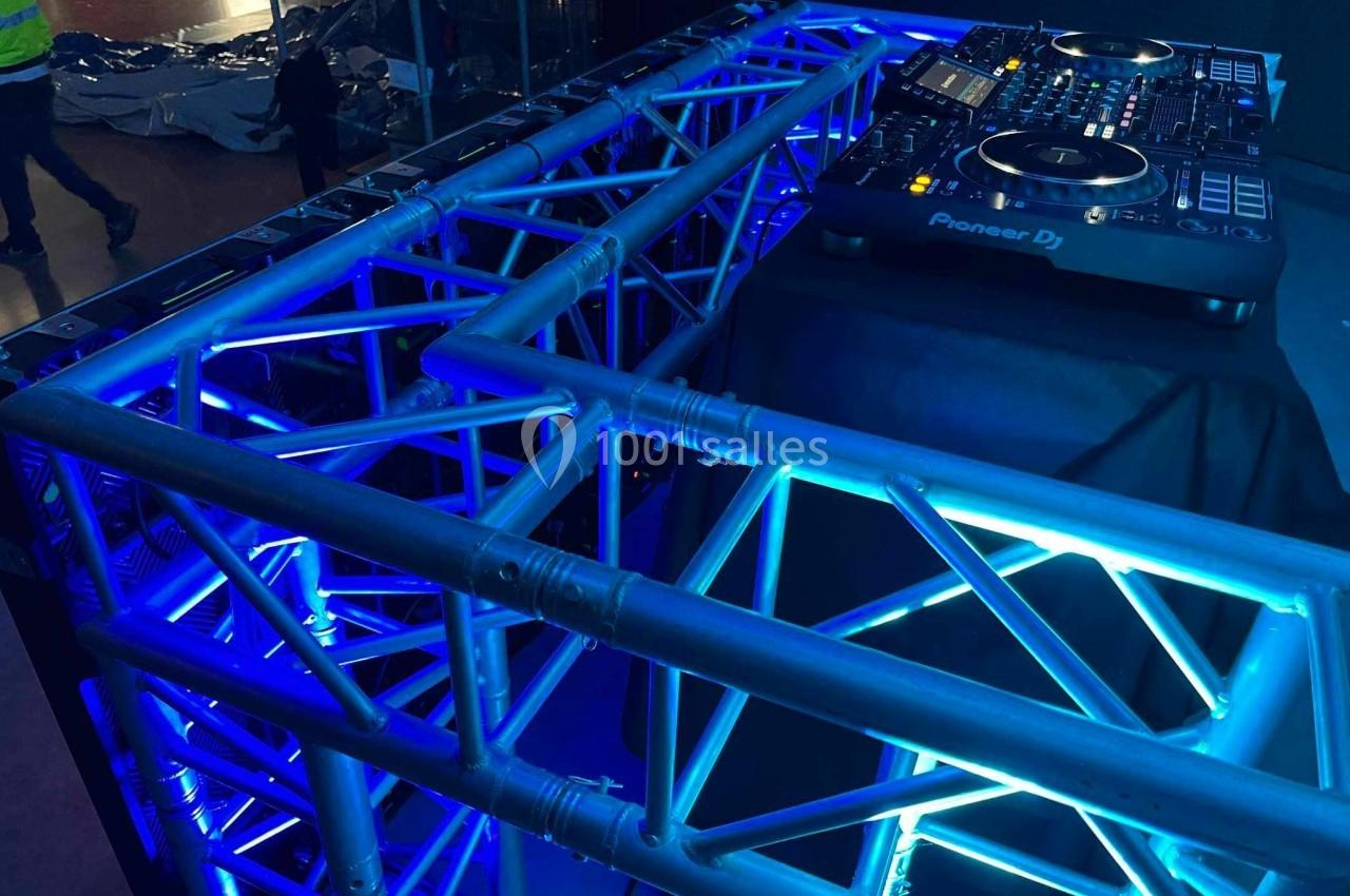 Structure métallique éclairée en bleu avec une table de mixage Pioneer DJ posée sur un support noir.