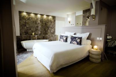 Miniature ADELAÏDE Chambre lumineuse avec lit double, fauteuil en bois, baignoire blanche et grande fenêtre donnant sur l'extérieur.