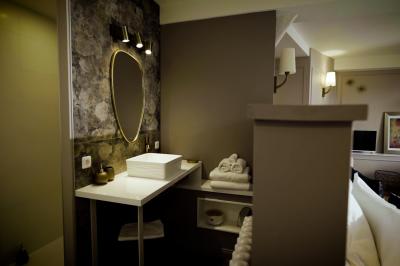 Miniature ADELAÏDE SALLE DE BAIN Chambre lumineuse avec lit double, fauteuil en bois, baignoire blanche et grande fenêtre donnant sur l'extérieur.