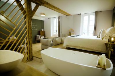 Miniature ALEXANDINE BAIGNOIRE POUR 2 Chambre lumineuse avec lit double, fauteuil en bois, baignoire blanche et grande fenêtre donnant sur l'extérieur.