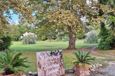 Miniature BIENVENUE A NOS MARIES Chambre lumineuse avec lit double, fauteuil en bois, baignoire blanche et grande fenêtre donnant sur l'extérieur.