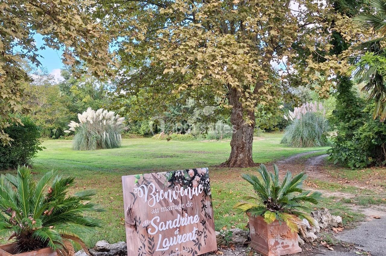 Panneau de bienvenue décoratif devant un parc verdoyant avec arbres, plantes et allée en arrière-plan.
