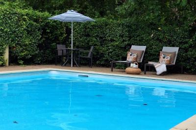 Miniature CHACUN SON ESPACE AU BORD DE LA PISCINE Chambre lumineuse avec lit double, fauteuil en bois, baignoire blanche et grande fenêtre donnant sur l'extérieur.