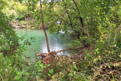 Miniature LA CHUTE D'EAU DU DEVERSOIR Chambre lumineuse avec lit double, fauteuil en bois, baignoire blanche et grande fenêtre donnant sur l'extérieur.