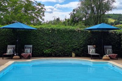 Miniature LA PISCINE Chambre lumineuse avec lit double, fauteuil en bois, baignoire blanche et grande fenêtre donnant sur l'extérieur.