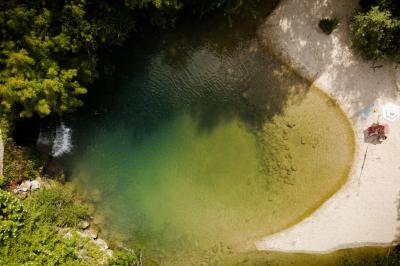 Miniature LA PLAGE Chambre lumineuse avec lit double, fauteuil en bois, baignoire blanche et grande fenêtre donnant sur l'extérieur.