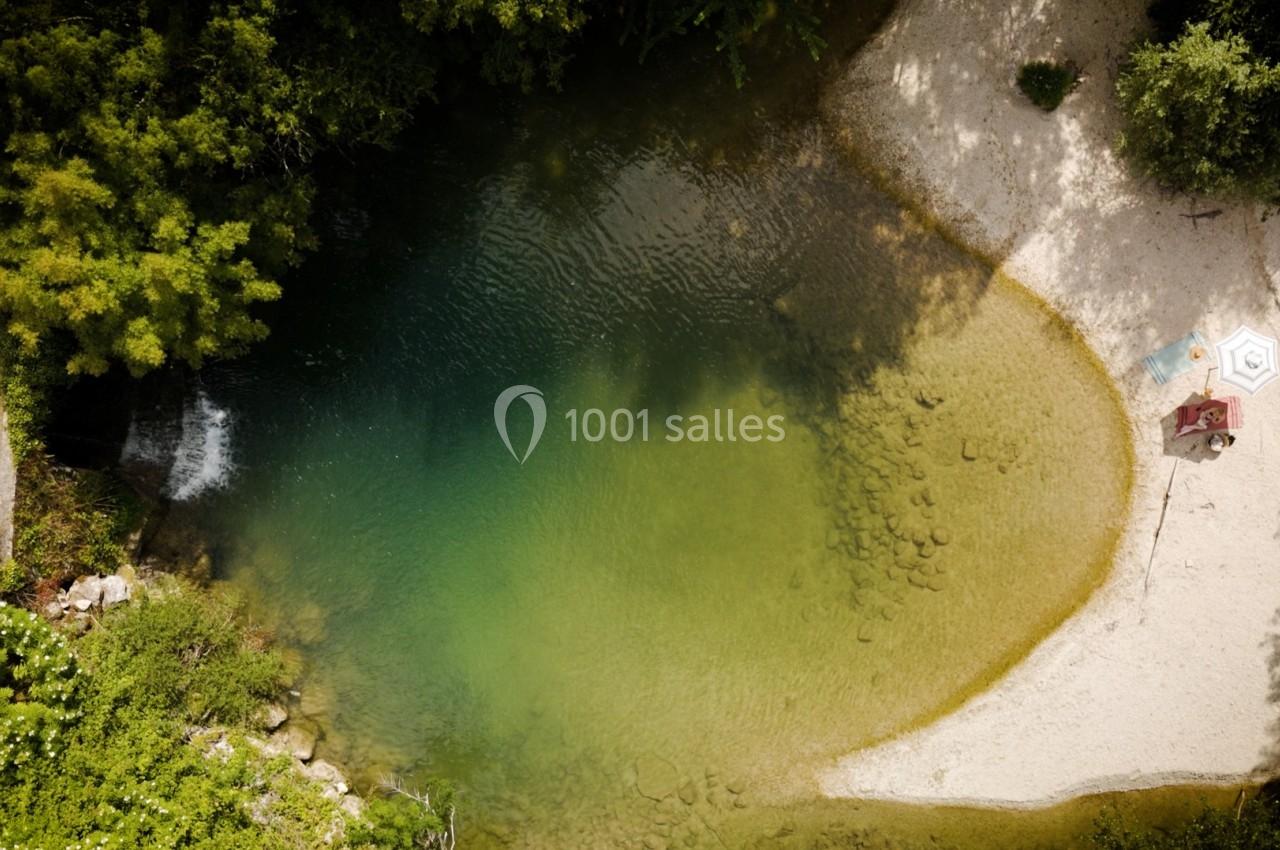 Vue aérienne d'une petite plage de sable bordant une rivière aux eaux claires entourée de végétation dense.
