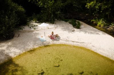 Miniature LA PLAGE Chambre lumineuse avec lit double, fauteuil en bois, baignoire blanche et grande fenêtre donnant sur l'extérieur.