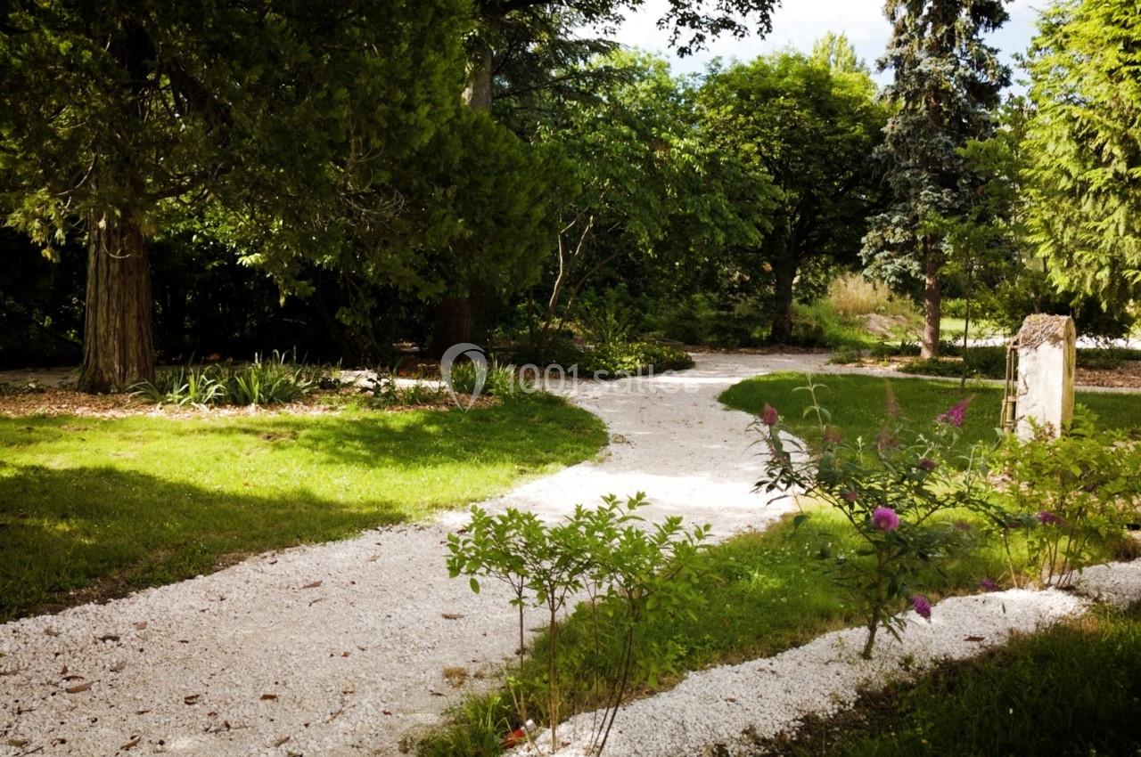 Allée sinueuse en gravier traversant un jardin verdoyant avec arbres et arbustes sous une lumière naturelle.