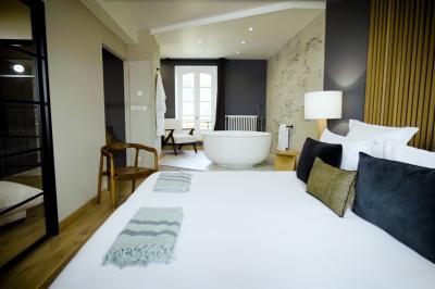 Miniature VICTORIA Chambre lumineuse avec lit double, fauteuil en bois, baignoire blanche et grande fenêtre donnant sur l'extérieur.