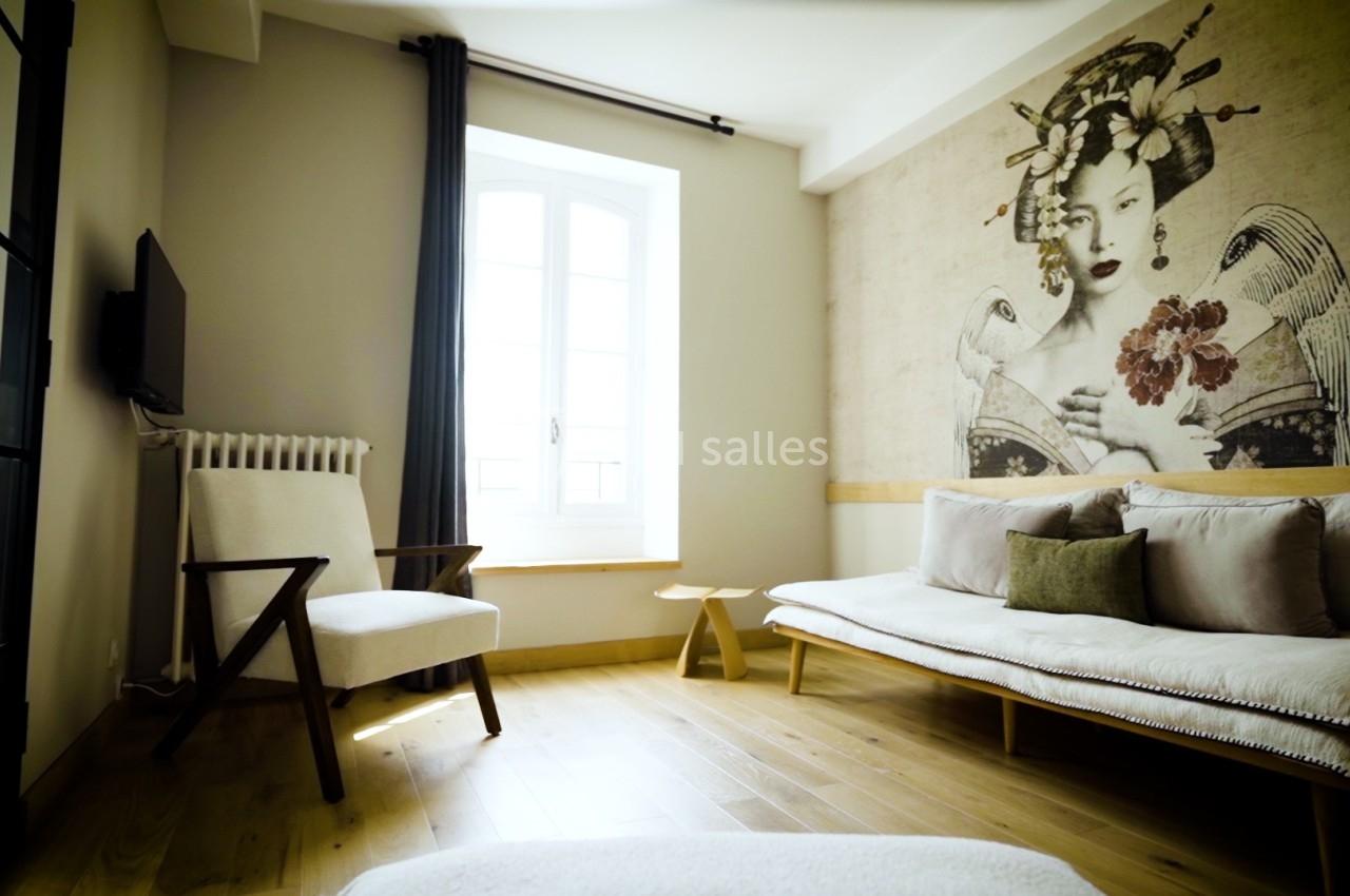 Salon lumineux avec parquet, canapé clair, fauteuil, table basse et mur décoré d'une fresque artistique.