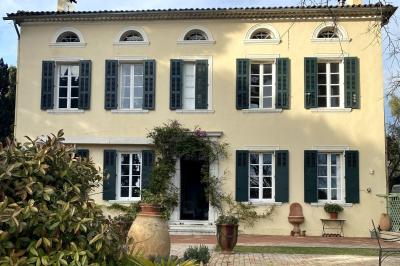 Façade d'une maison provençale jaune à volets verts, éclairée par le soleil couchant, avec une cour pavée et des plantes.