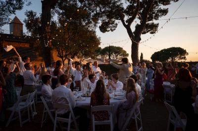 Façade d'une maison provençale jaune à volets verts, éclairée par le soleil couchant, avec une cour pavée et des plantes.