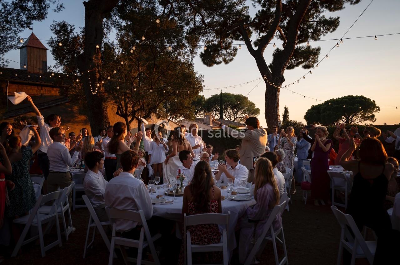 Groupe de personnes célébrant un événement en plein air au coucher du soleil, entourées de guirlandes lumineuses.