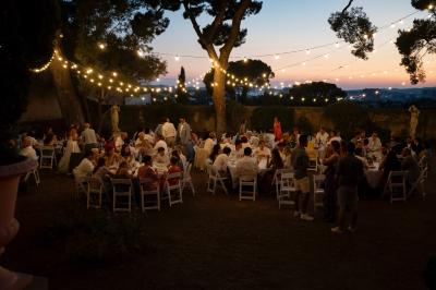 Façade d'une maison provençale jaune à volets verts, éclairée par le soleil couchant, avec une cour pavée et des plantes.