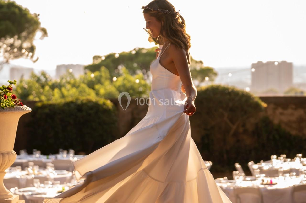 Femme en robe blanche dansant en extérieur au coucher du soleil, entourée de tables dressées et de verdure.