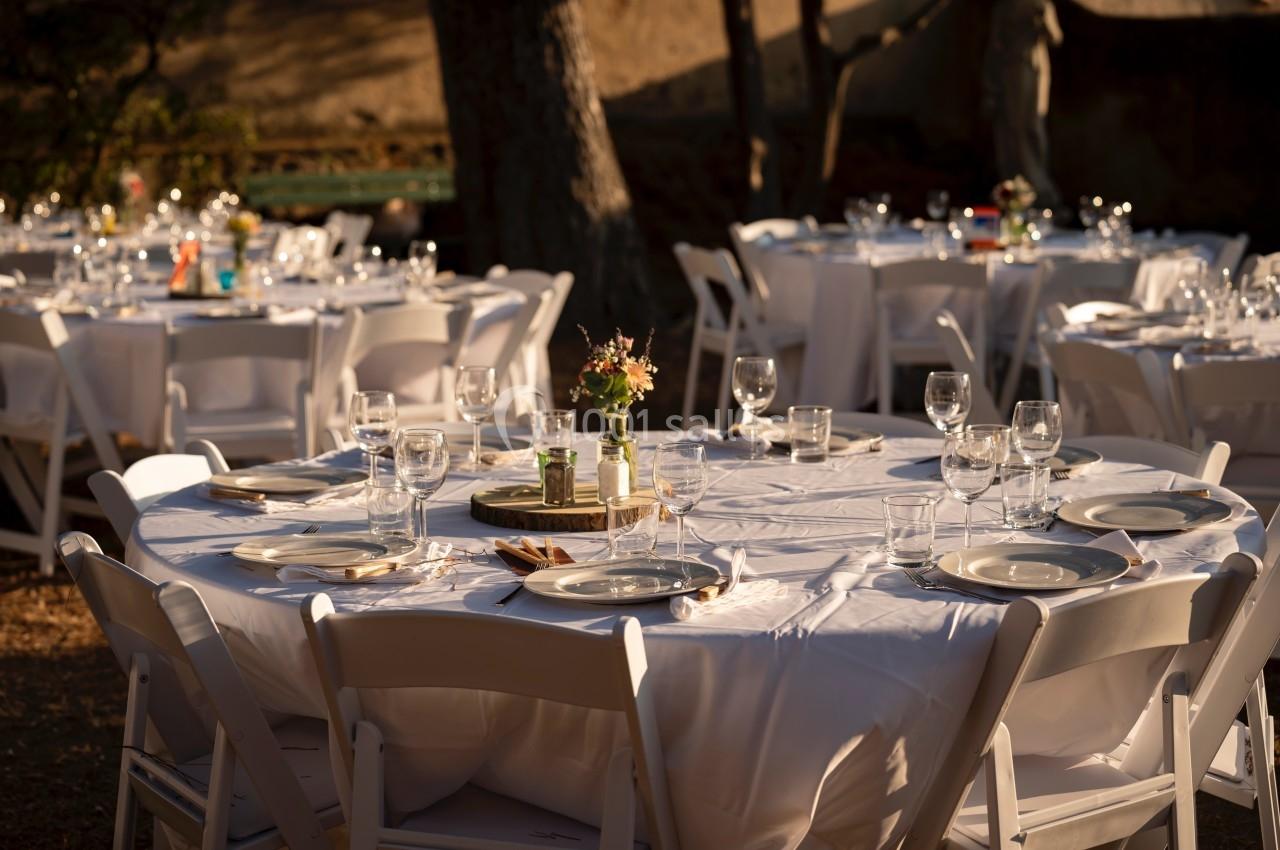 Tables rondes dressées avec nappes blanches, vaisselle et verres, disposées en extérieur sous une lumière douce.