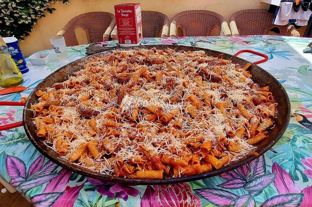 Plat de pâtes rigatoni en sauce tomate, garni de fromage râpé, servi dans une grande poêle sur une table colorée.
