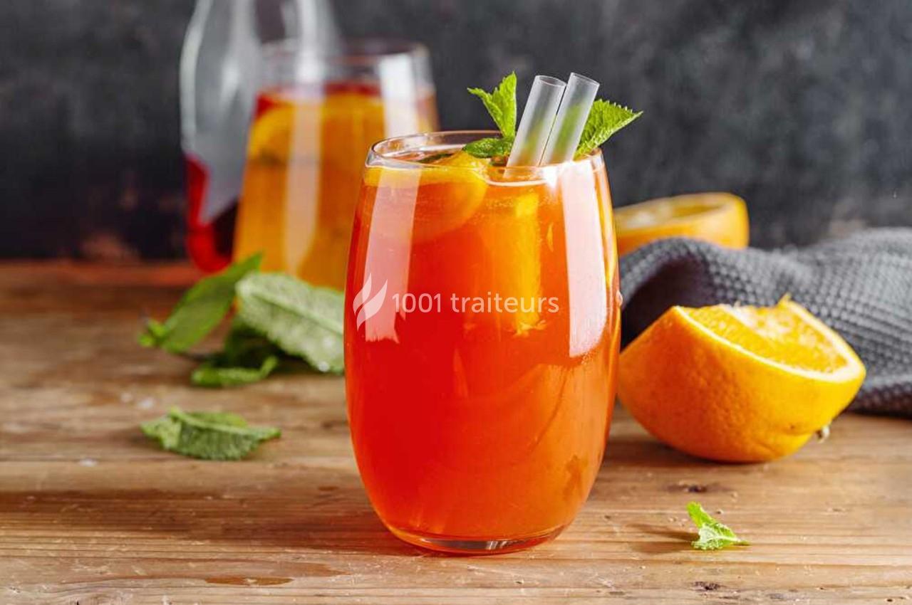 Verre de cocktail orange avec glaçons, tranches d'orange et menthe, posé sur une table en bois.