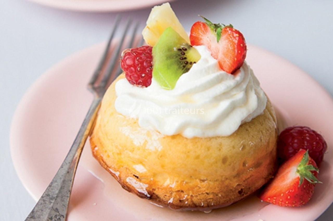 Gâteau individuel garni de chantilly, fraises, kiwi, framboises et ananas, présenté sur une assiette rose avec une…
