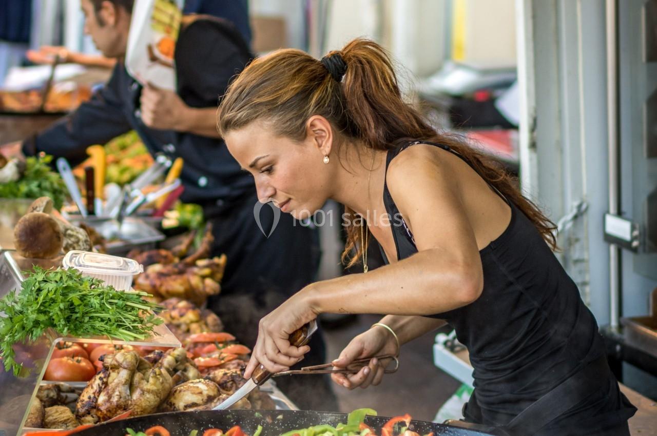 Une femme cuisine des légumes et de la viande sur un stand de marché en plein air.