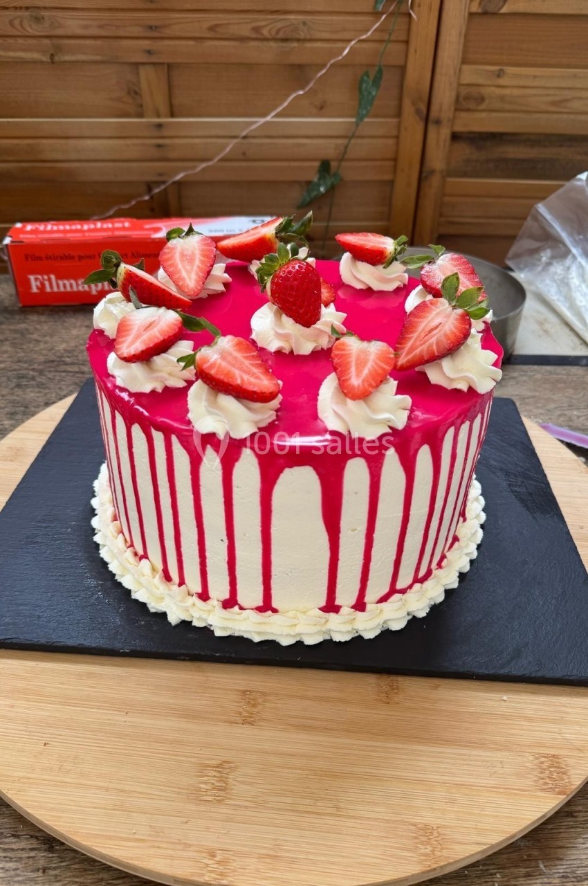 Gâteau décoré de glaçage rose coulant, de fraises fraîches et de rosettes de crème, posé sur une ardoise noire.